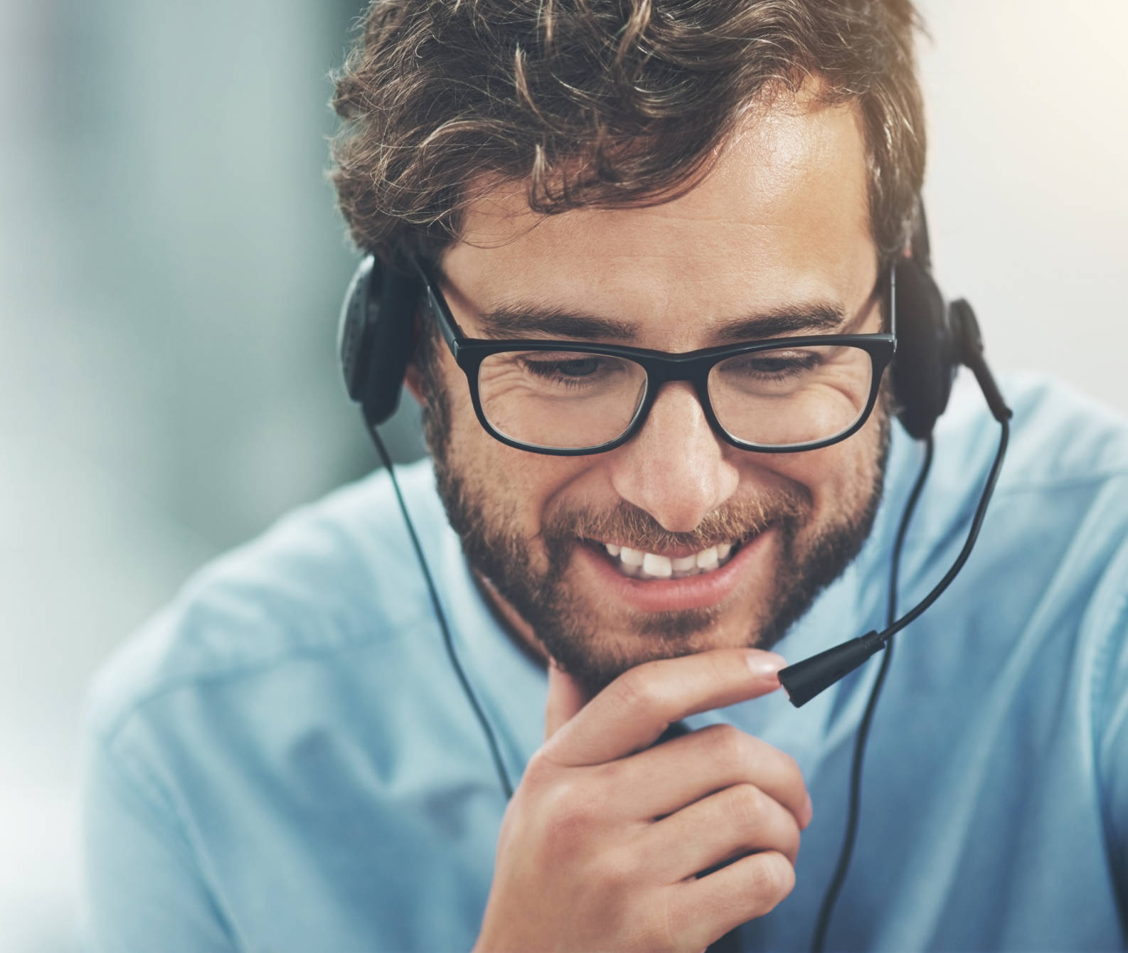 Customer service man with glasses and headset leaning forward with chin in hands and smiling